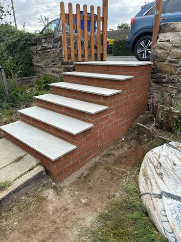 Newly constructed brick stairs with light stone treads and wooden gate on top.