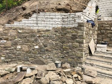Stone wall construction with mixed old and new bricks in progress.
