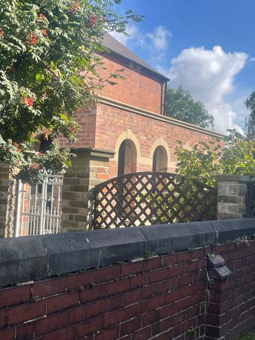 Brick house with arched windows behind a stone and metal fence on a sunny day.