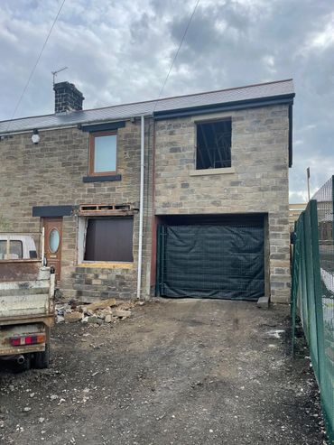Stone house under renovation with boarded windows and a truck outside.