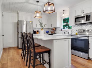 Modern white kitchen with wooden stools and stainless steel appliances.
