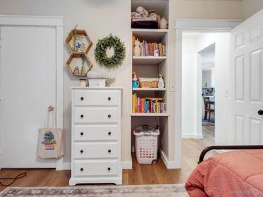 Cozy bedroom corner with white dresser, bookshelf, and warm wooden floor.
