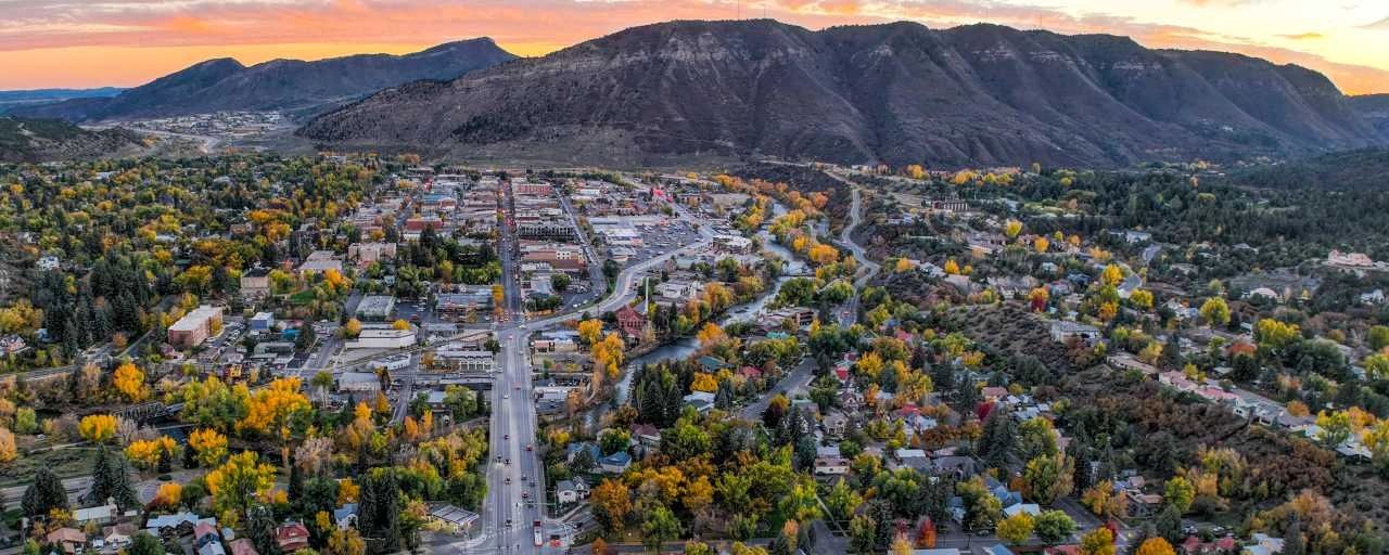 A town nestled in a valley with autumn foliage and mountains at sunset.