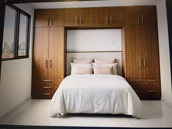 Modern bedroom with built-in wooden wardrobes surrounding a neatly made bed.