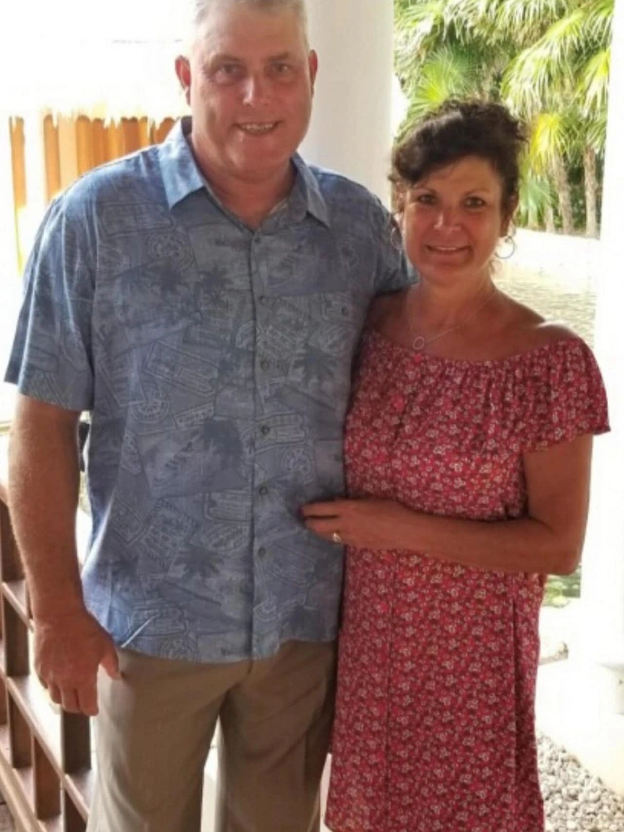 Smiling couple posing together outdoors with greenery in the background.
