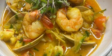 A bowl of seafood soup with shrimp and clams.