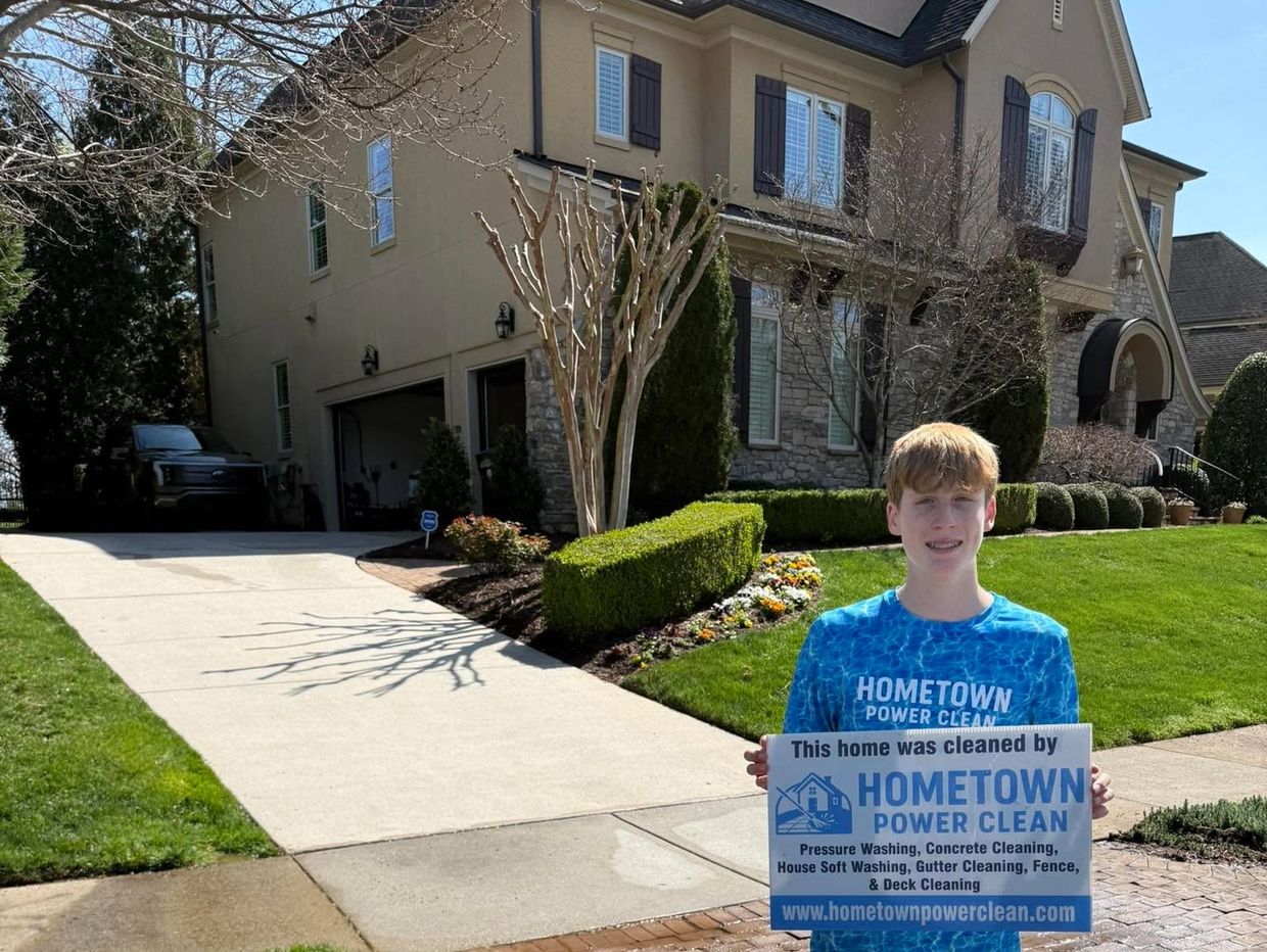 Young person holding a sign for Hometown Power Clean in front of a clean driveway and house.