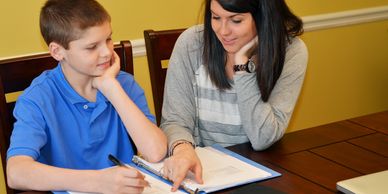 A woman helps a boy with his homework at a table.