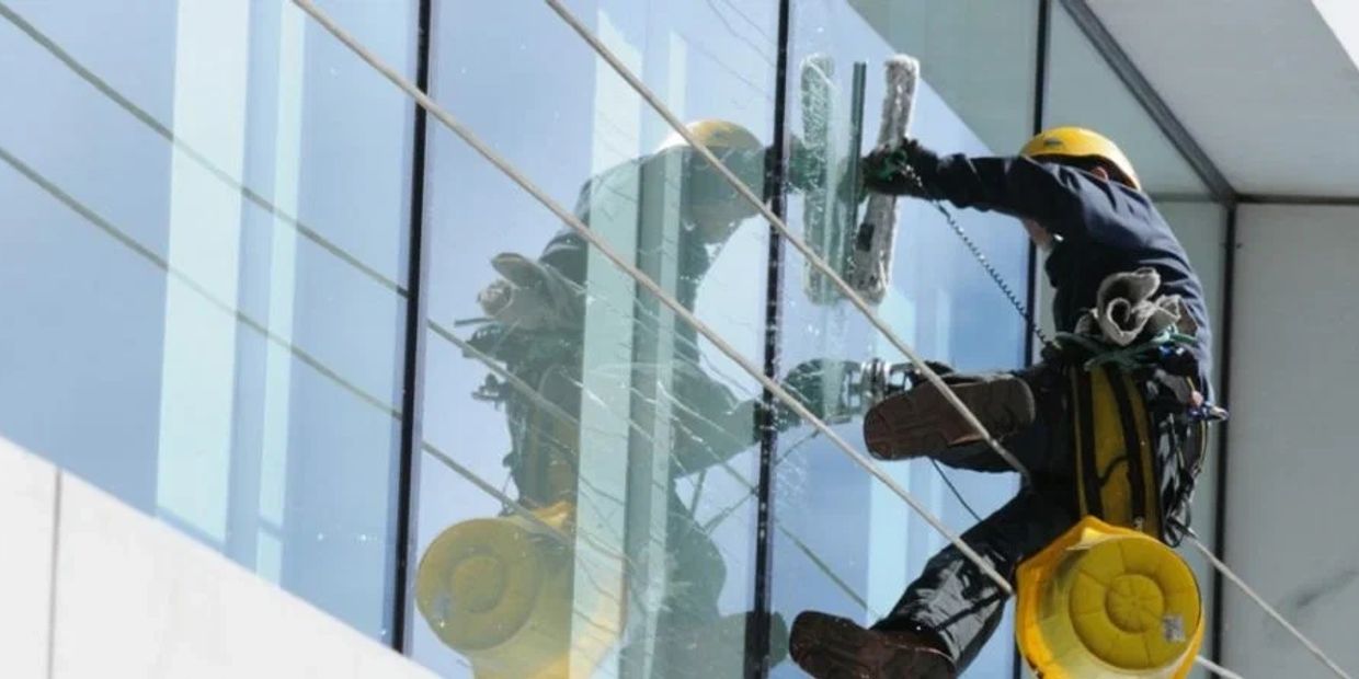 A worker cleaning tall glass windows with safety gear.