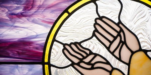 Stained glass window depicting praying hands with vibrant purple and yellow accents.