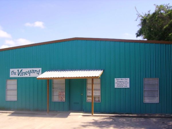 Exterior of a teal building named 'the Vineyard' with a small porch and signage.