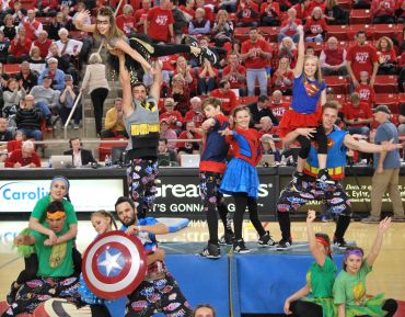 Group in superhero costumes performing acrobatic cheer routine.