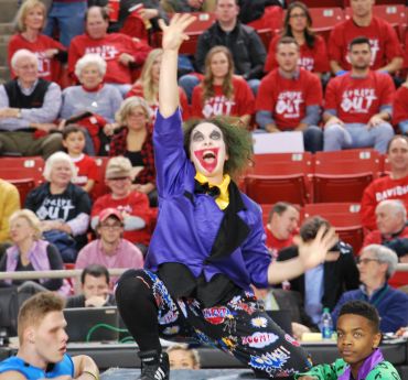 Clown entertaining at a sports event with an enthusiastic crowd.