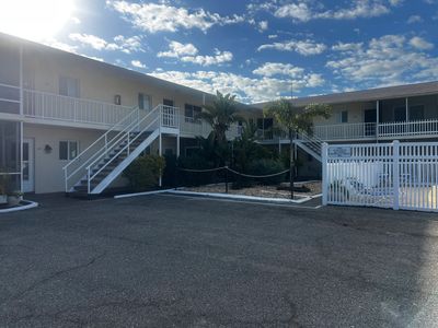 Two-story motel with outdoor staircases and a gated pool area under a blue sky.
