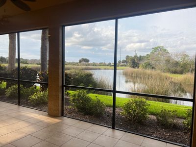 Scenic lake view from a screened patio with greenery and cloudy sky.