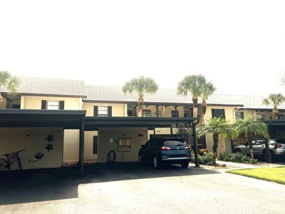 Townhouses with carports and palm trees in front under bright sunlight.