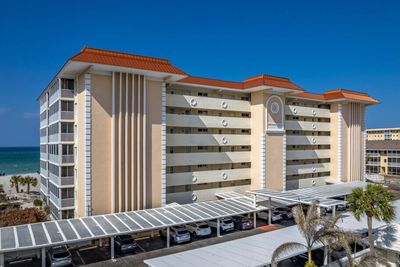 Beachside condominium building with covered parking under a clear blue sky.