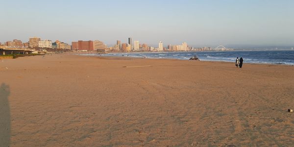 Spacious beach with city skyline and two people walking.