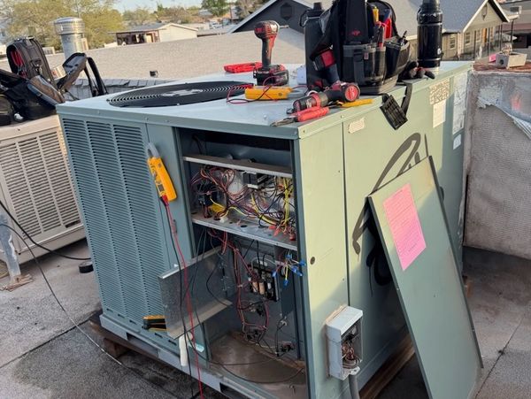Technician repairing an outdoor HVAC unit with tools and wires visible.