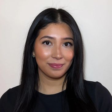 Young woman with long black hair smiling gently against a plain background.