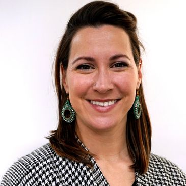Smiling woman with green earrings and a houndstooth jacket.