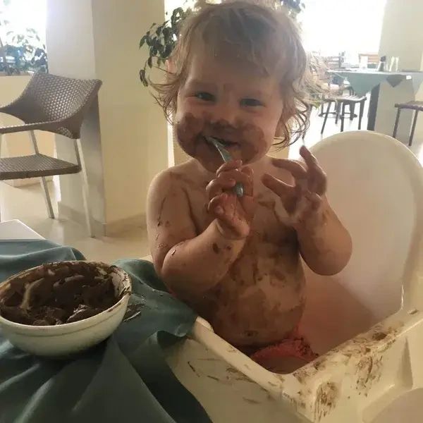 Young child sat in a highchair with a messy face from food.