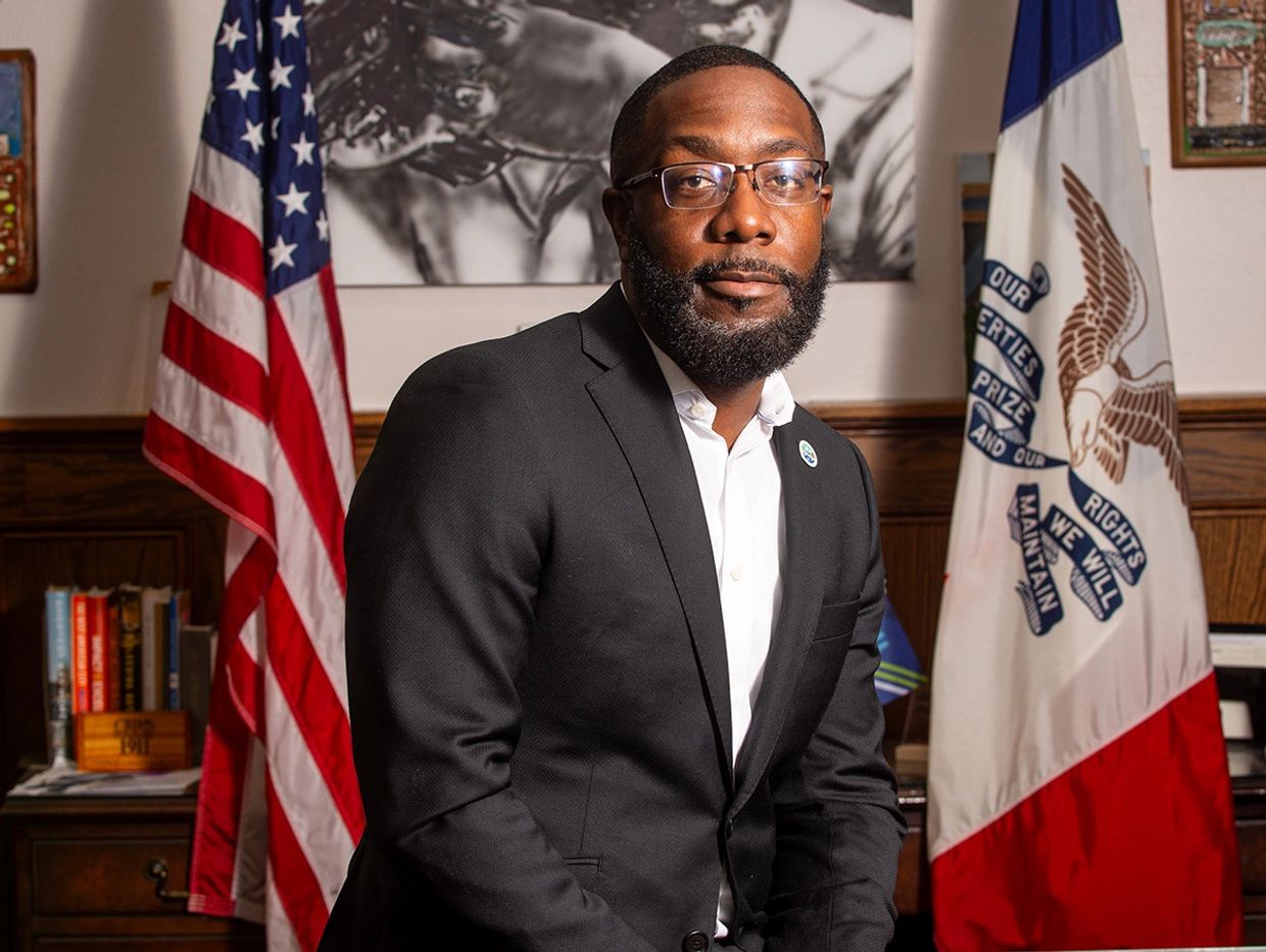 Man in suit posing with American and Iowa state flags in background.