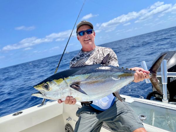 Man proudly holds a large tuna fish on a boat under a clear blue sky.