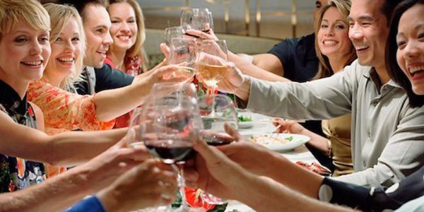 A group of friends happily toasting with wine glasses at a dinner table.