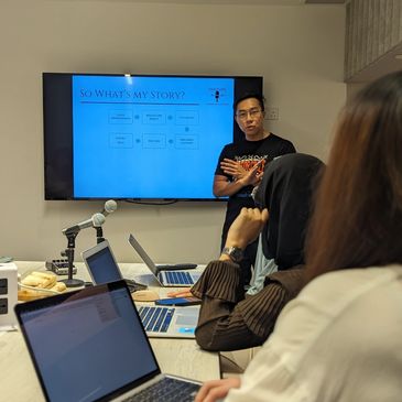 Person presenting a story on a screen to an attentive audience with laptops.