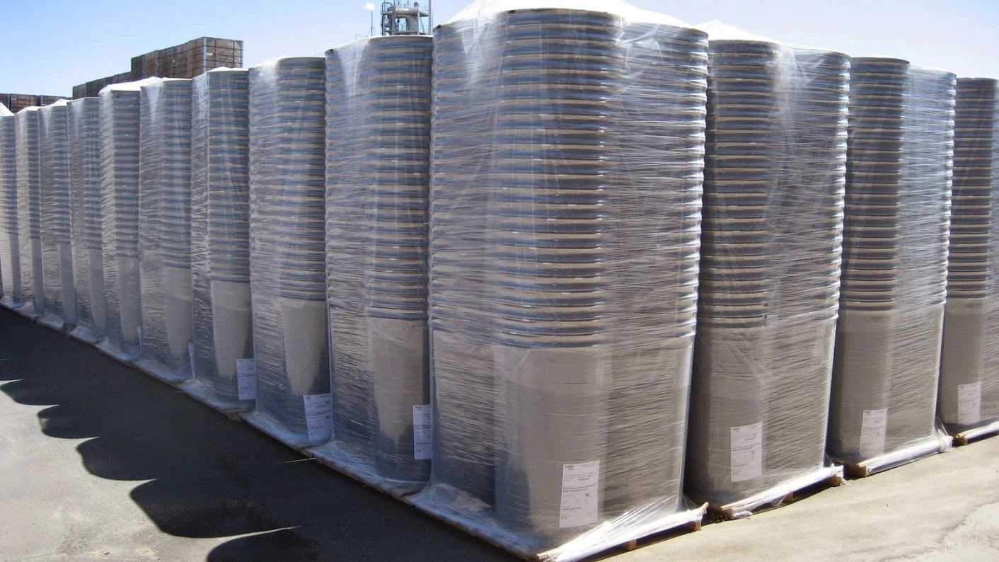 Rows of large cylindrical containers wrapped in plastic on pallets outdoors.