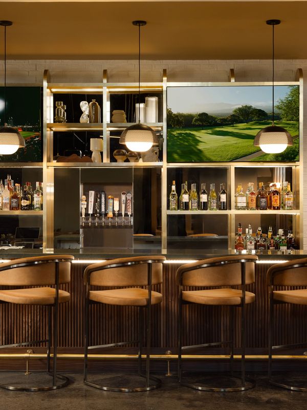 Elegant bar with leather stools, pendant lights, and a TV displaying a golf course.