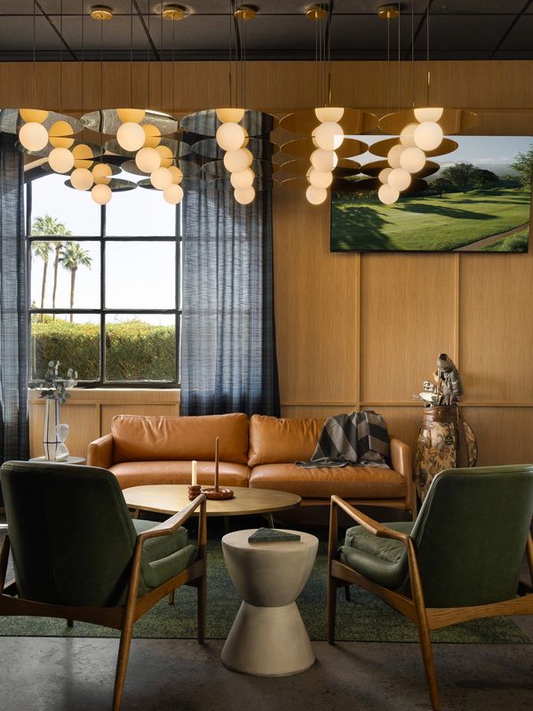 Cozy living room with leather sofa, green chairs, and modern lighting.