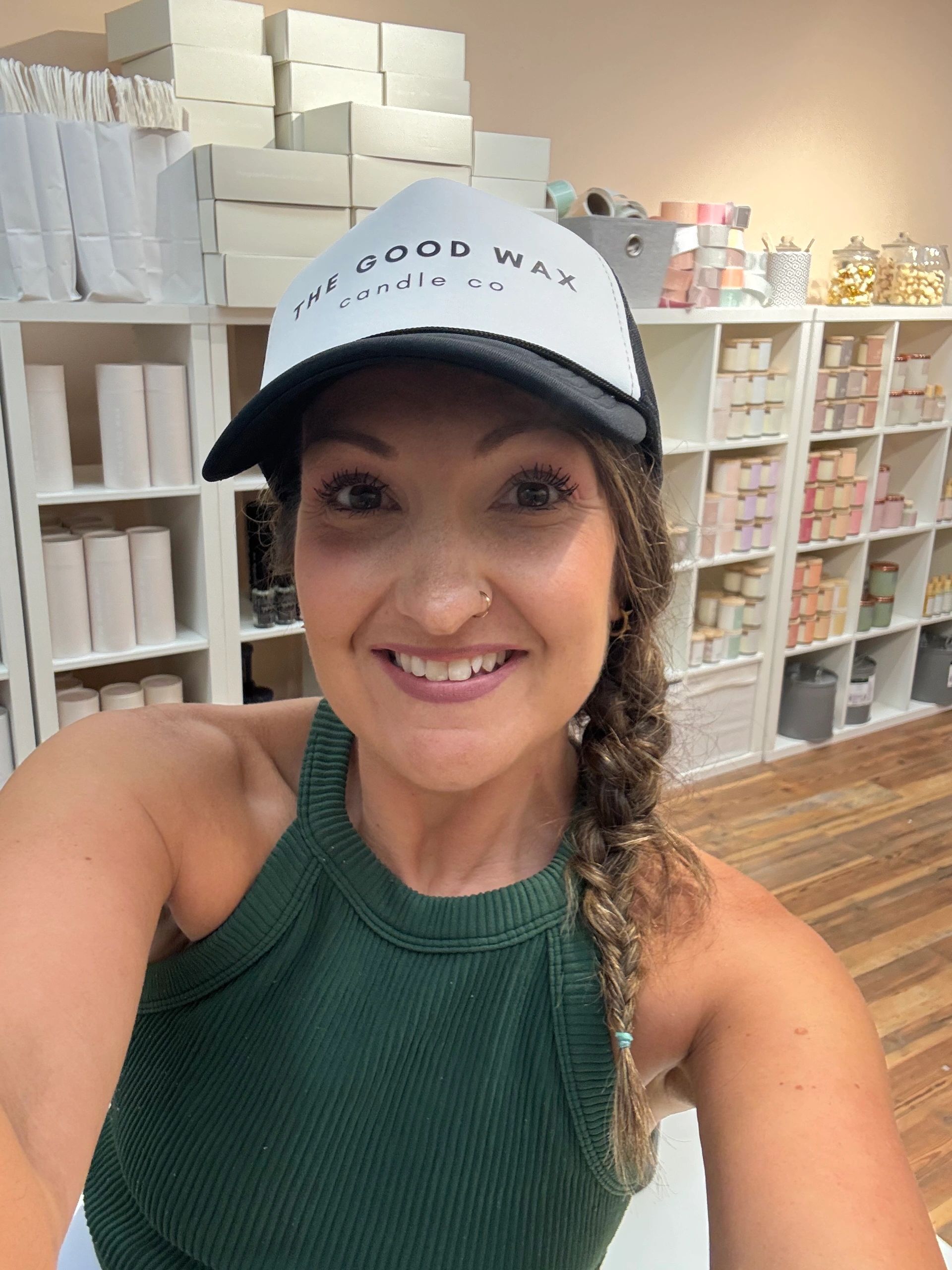 Smiling woman wearing a 'The Good Wax Candle Co' hat in a candle shop.