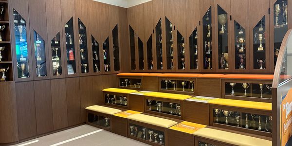 Wooden trophy cabinets with cushioned seating and numerous trophies inside.