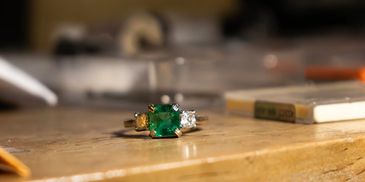 Emerald and diamond ring on wooden surface in soft light.