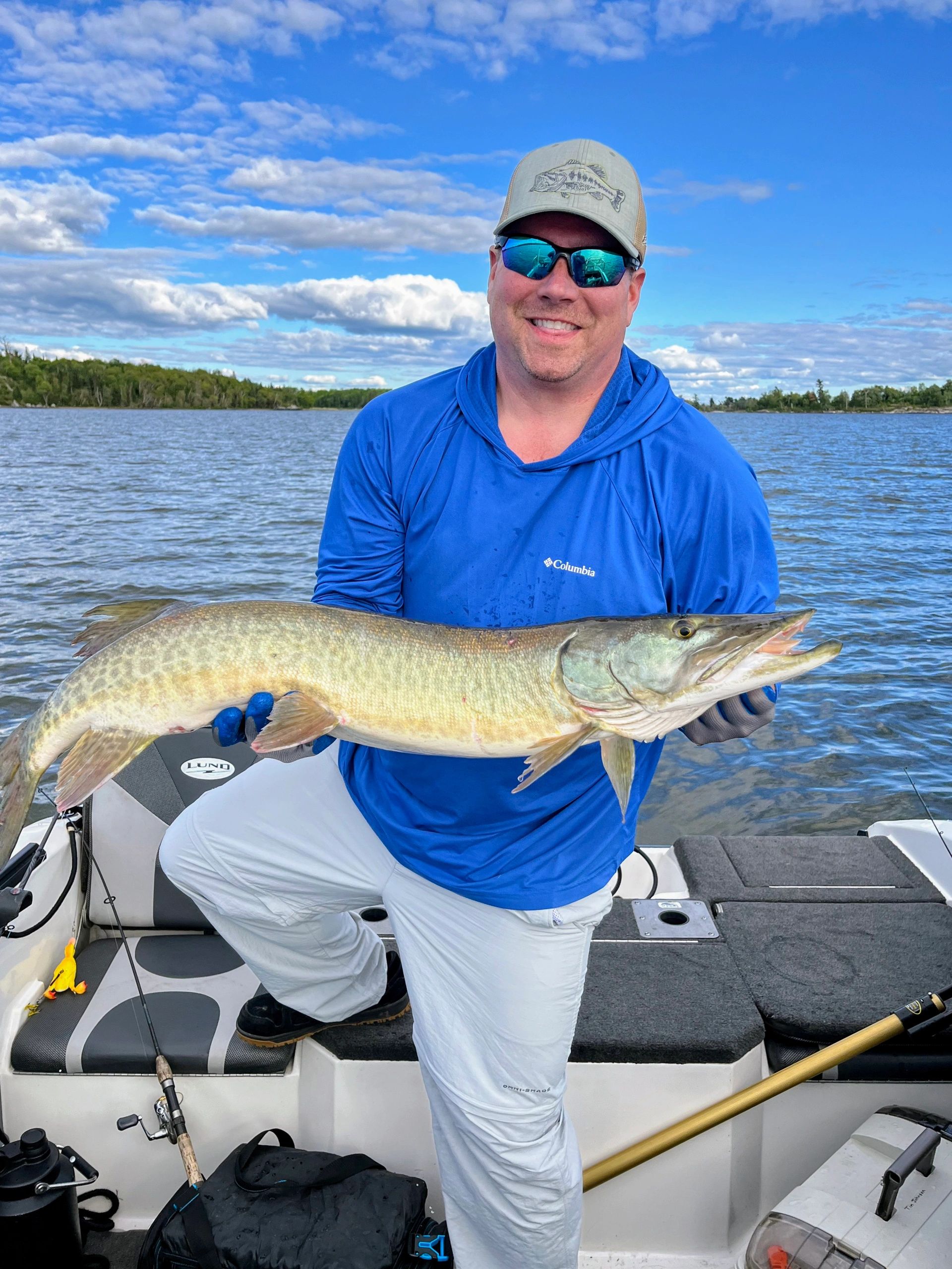 Man in blue holds a large fish on a boat under a blue sky.