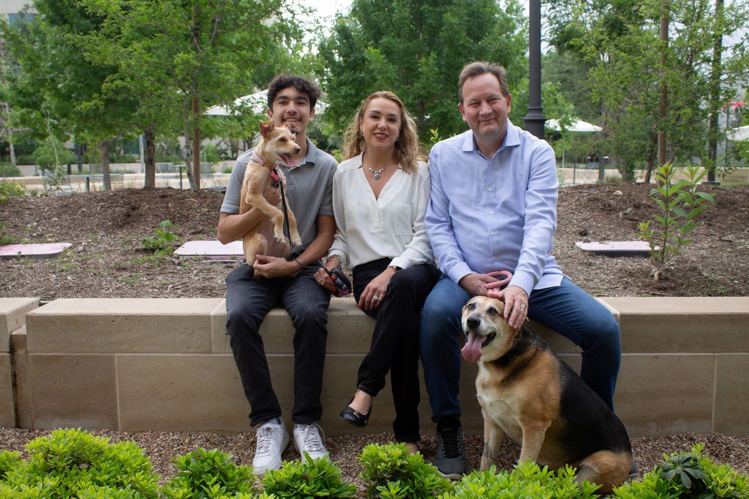 A family of three with two dogs sitting outdoors on a stone bench.