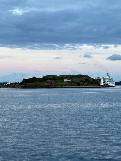 Small green island with a cruise ship docked beside it under a cloudy sky.