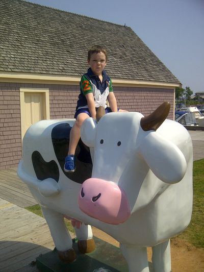 Boy sitting on a large cartoon cow sculpture outdoors.
