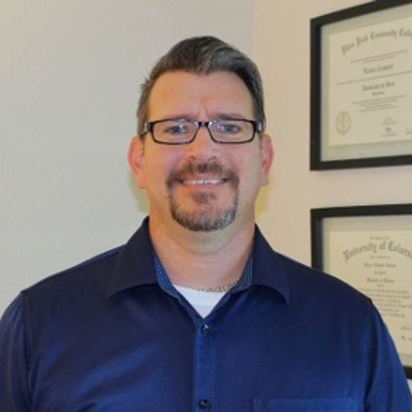 Man with glasses smiling in front of framed certificates.