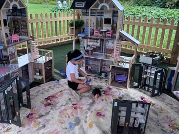 Little girl playing with a large barbie theme dollhouse under a gazebo.