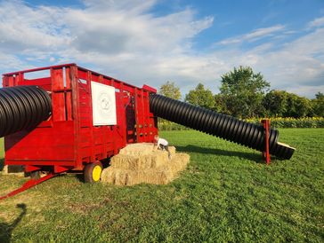 Children playing on a red farm structure with hay bales and slide tubes.