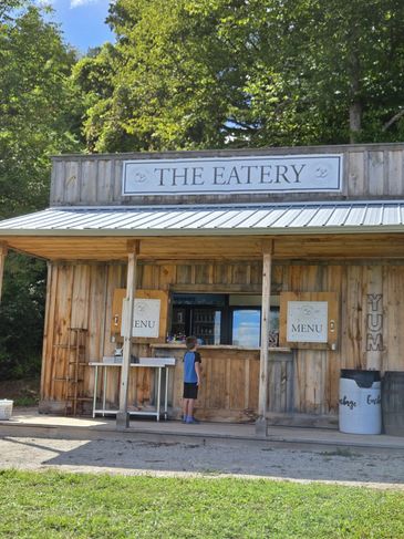 Child standing at wooden food shack called The Eatery.