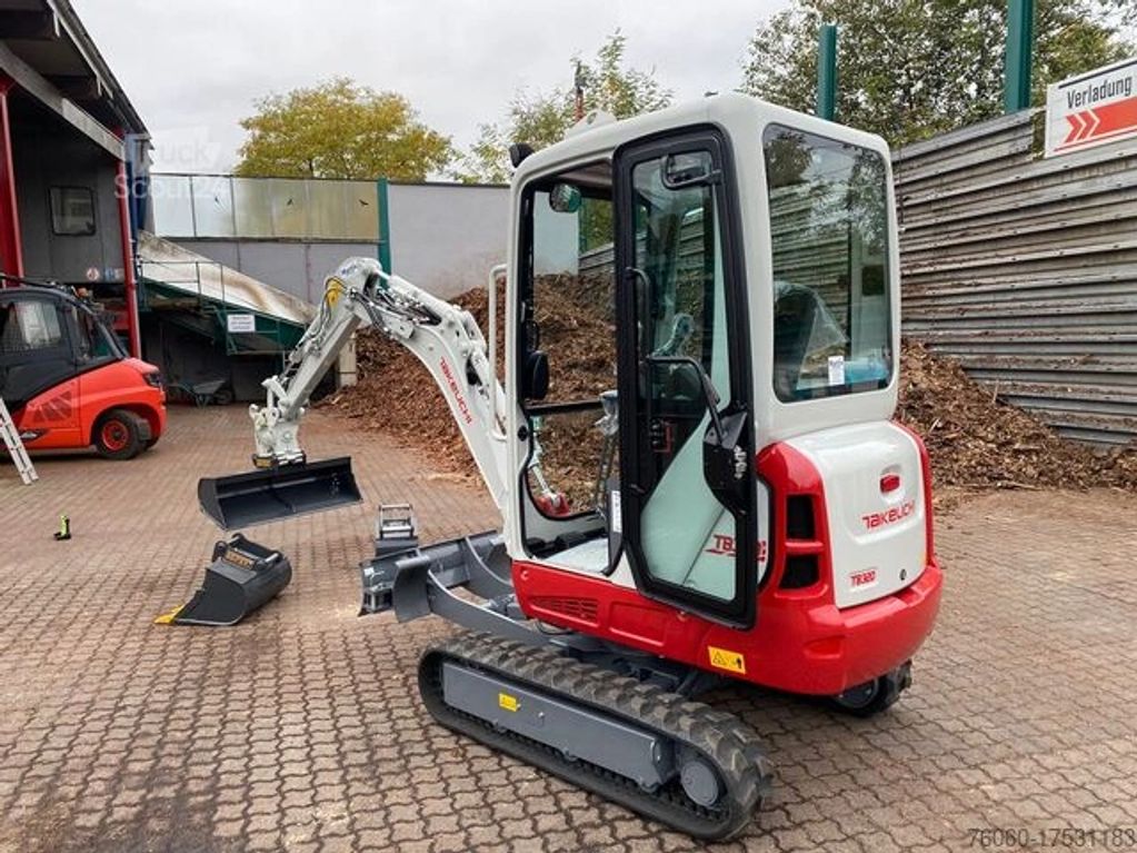 Compact Takeuchi mini excavator with glass cabin and open door on industrial pavement.