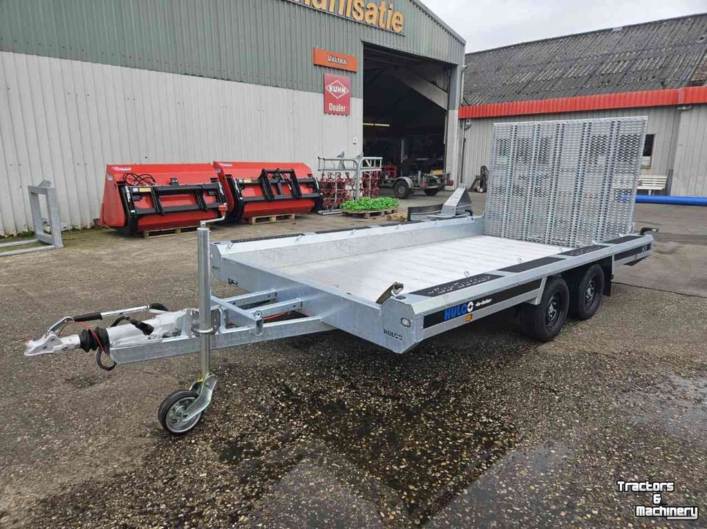 Metal flatbed trailer with loading ramps parked outside a machinery building.