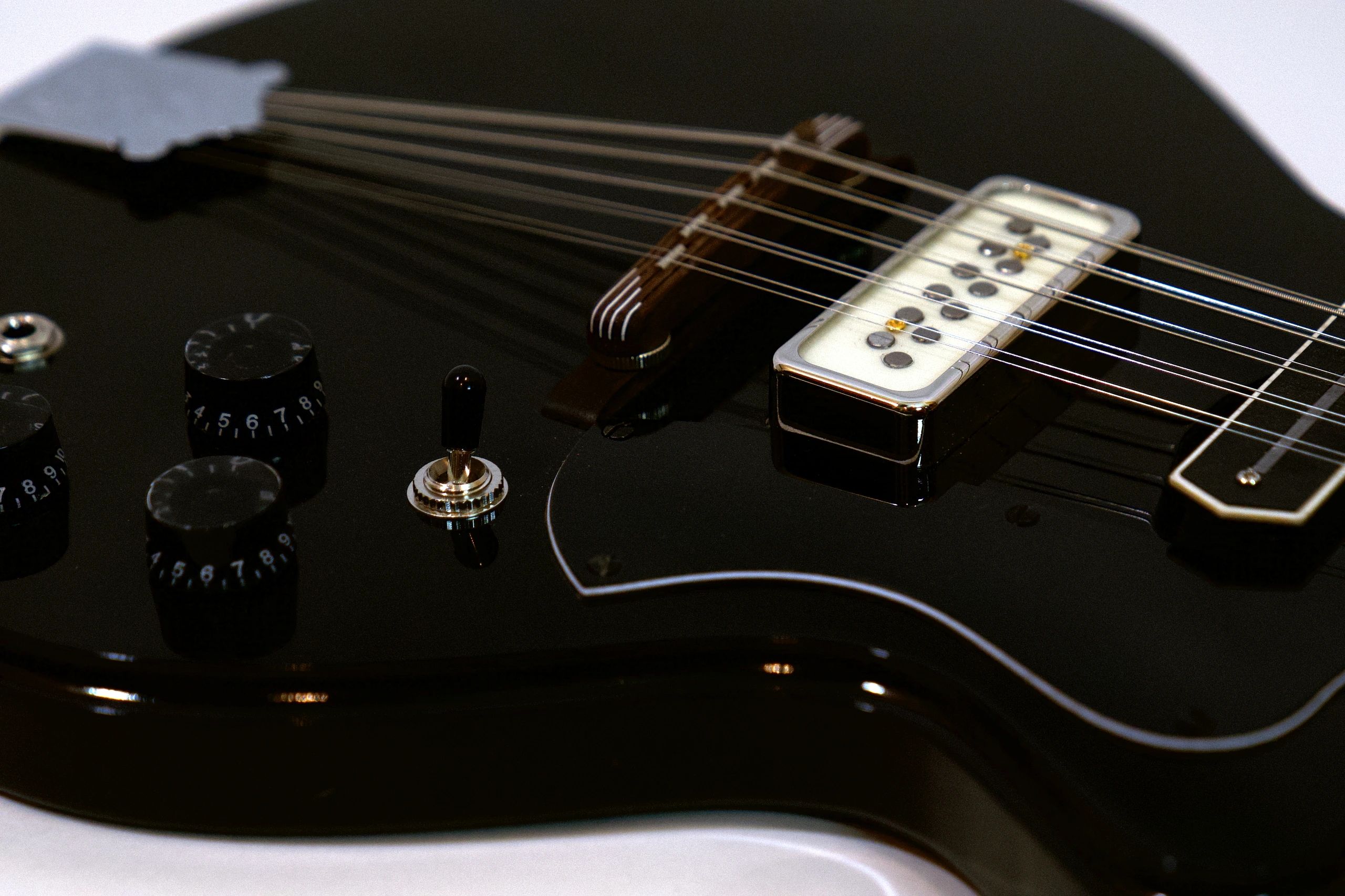 Close-up of a black electric guitar's strings, knobs, and switch.