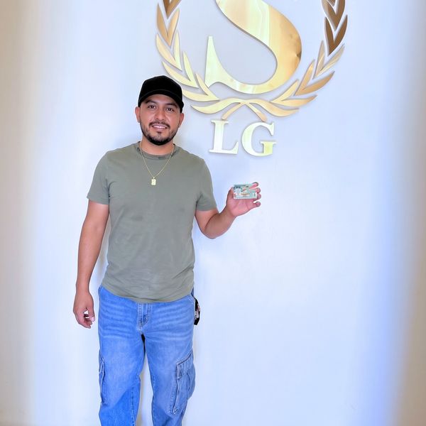 Man smiling, holding a card, standing by a logo on the wall.