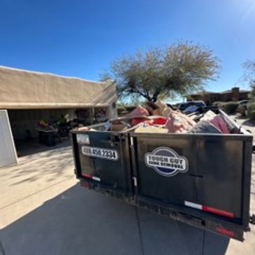 Dumpster filled with debris outside a house under clear sky.