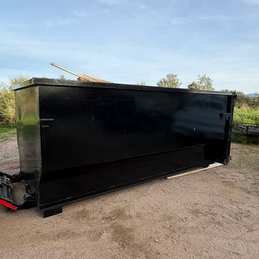 Large black metal dumpster outdoors on dirt ground.